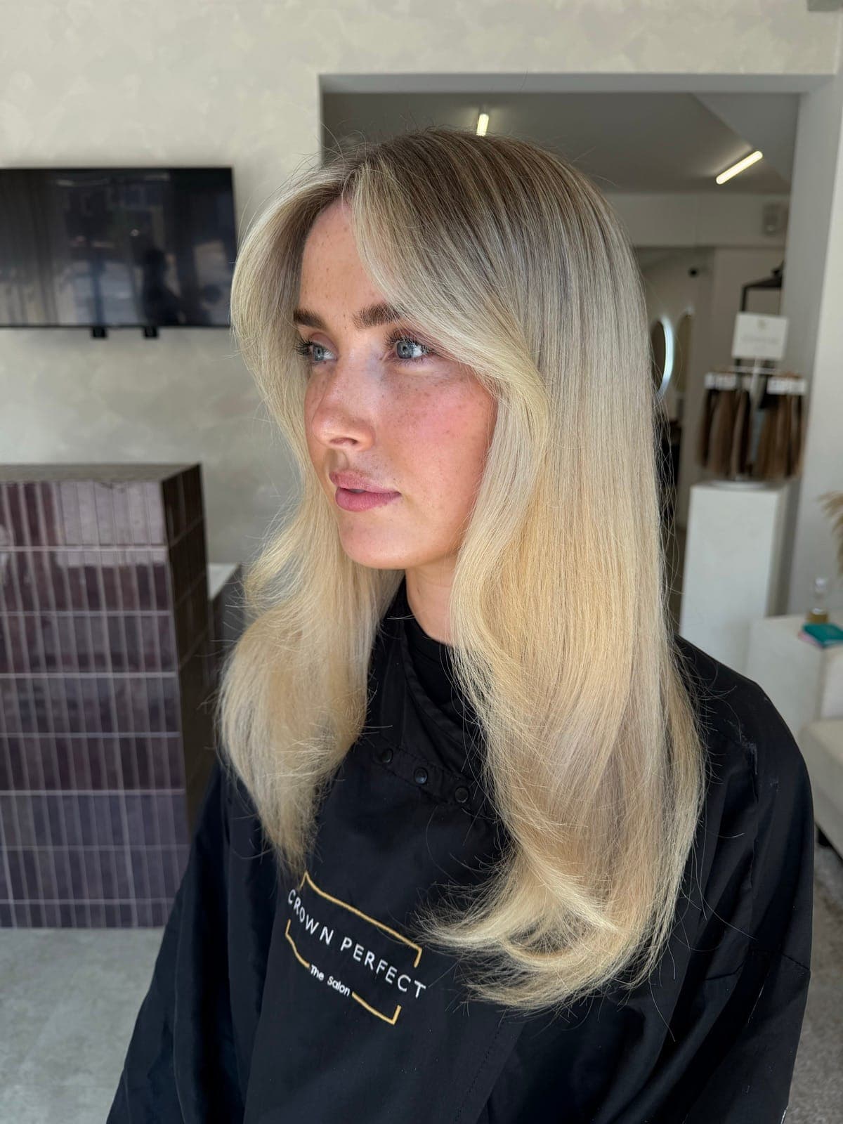 A client in profile with long, bright blonde hair in a smooth, glossy blow dry.