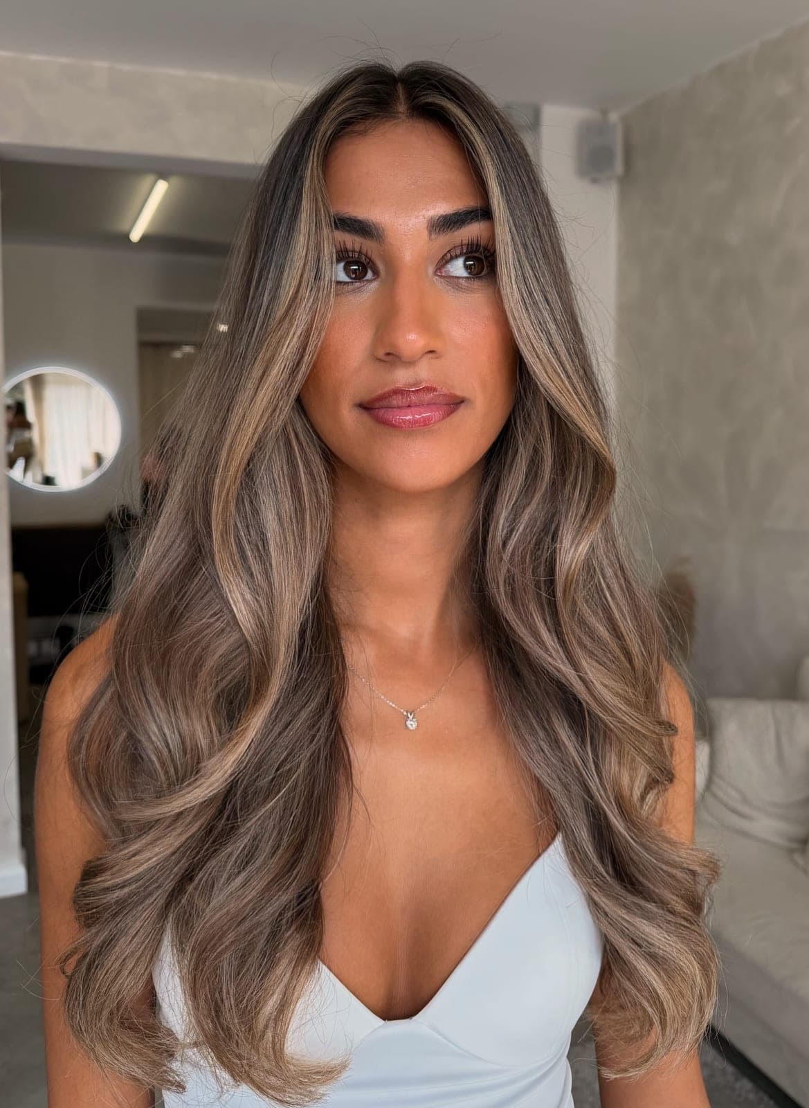 Long brunette with soft caramel balayage and face-framing lightness, worn in loose, glossy waves in the salon.