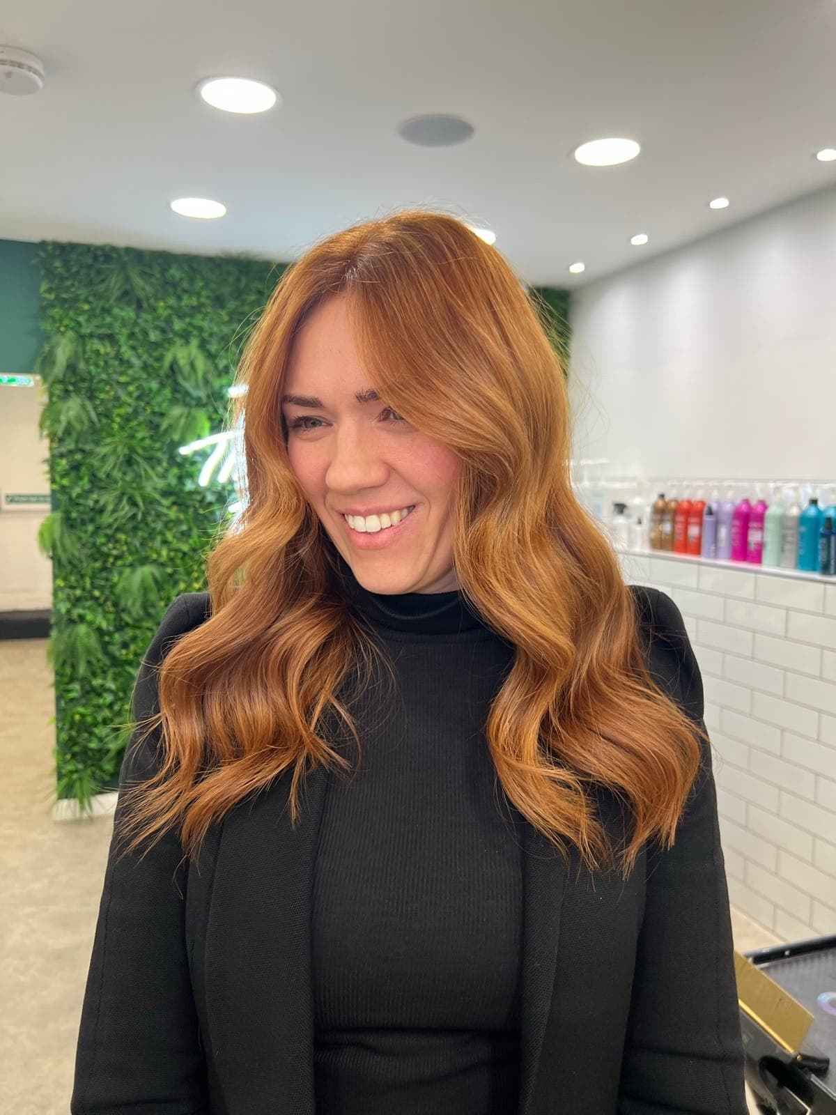 A smiling client with warm copper hair in soft waves, worn just past the shoulder.