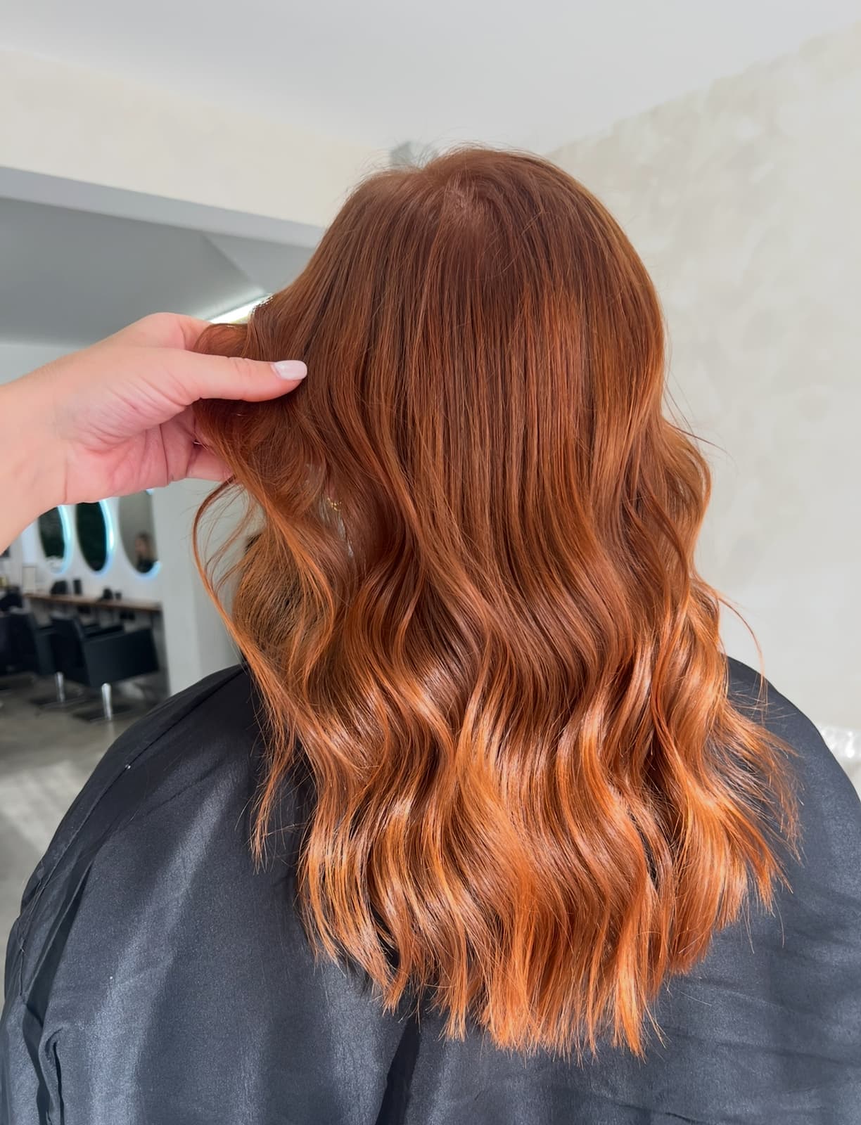Back view of long copper hair, hands in the hair, in the salon.