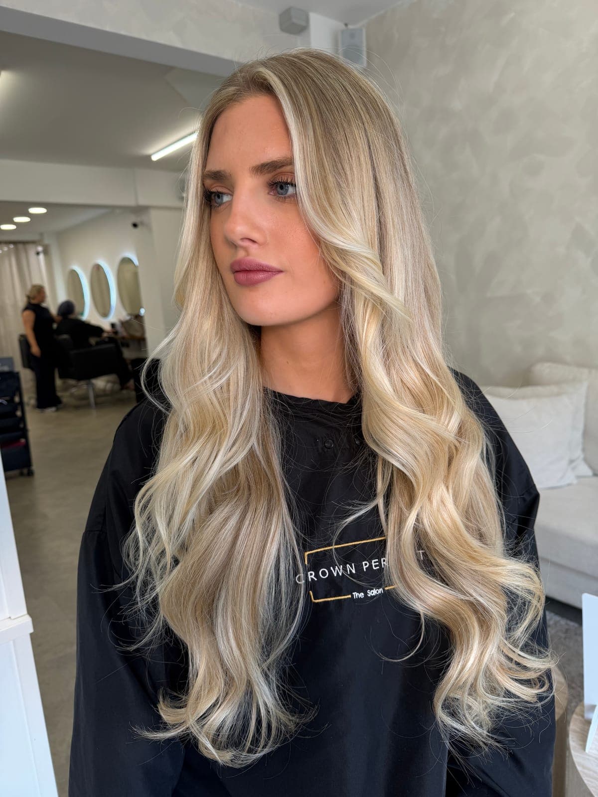 A long, flat blonde with darker roots refreshed into a brighter, dimensional blonde with face-framing pieces and soft waves, after